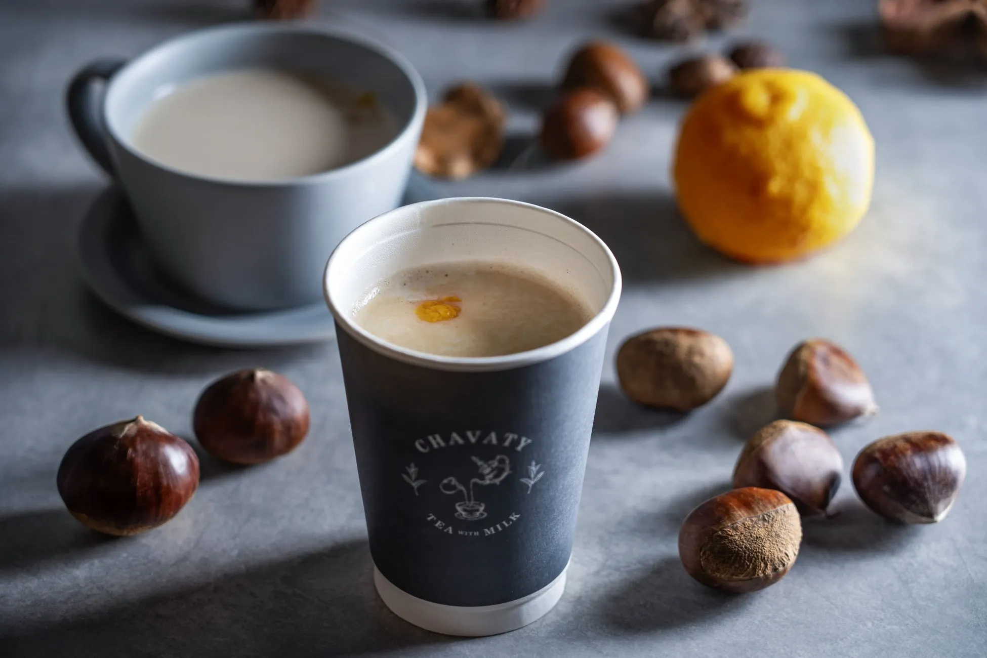 温かい飲み物と栗のクローズアップ写真。カップに入った飲み物、栗、レモンがテーブルに置かれている。